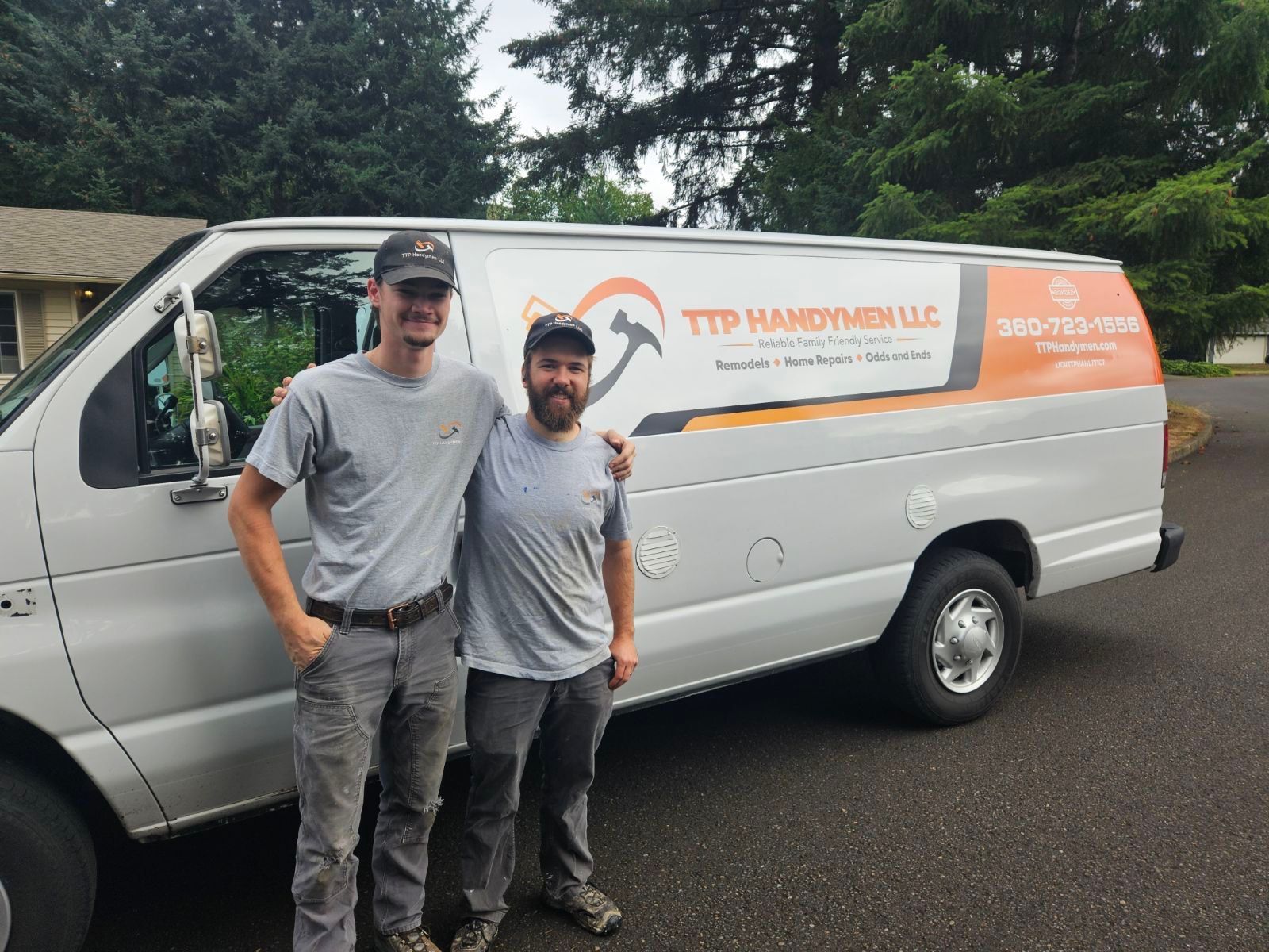 Two men standing beside a white service van with orange lettering on a wet street.