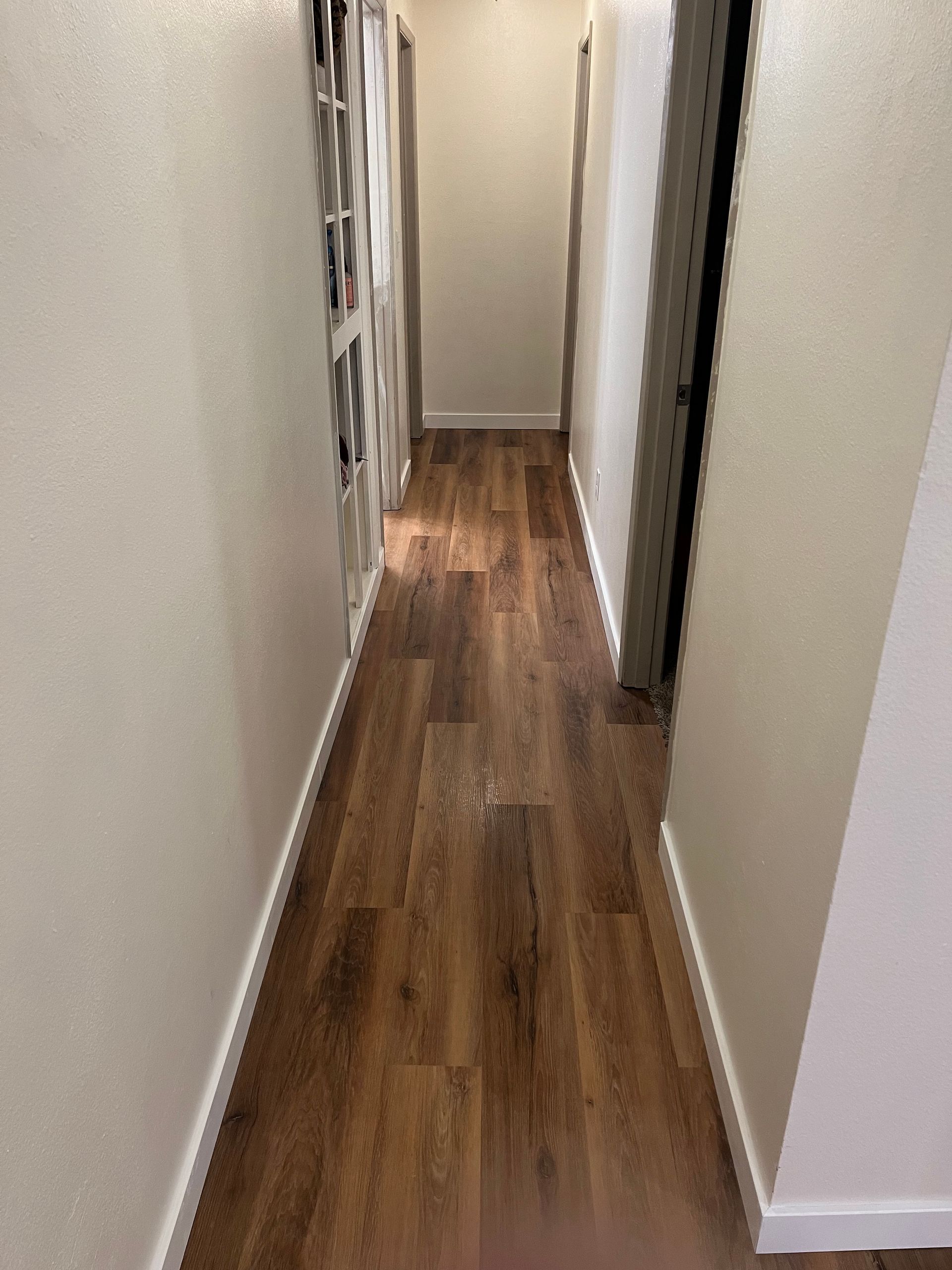 Narrow hallway with wood floors, white walls, and framed photos on the left.
