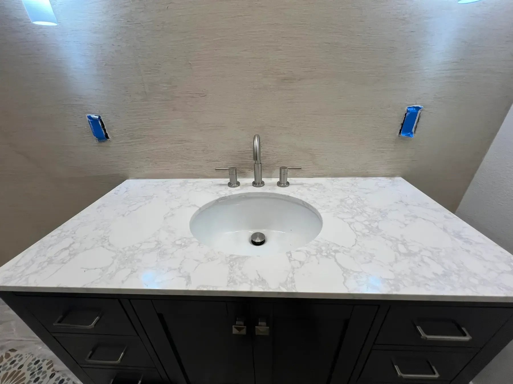 Bathroom vanity with white marble countertop, oval sink, chrome faucet, and dark cabinet below.
