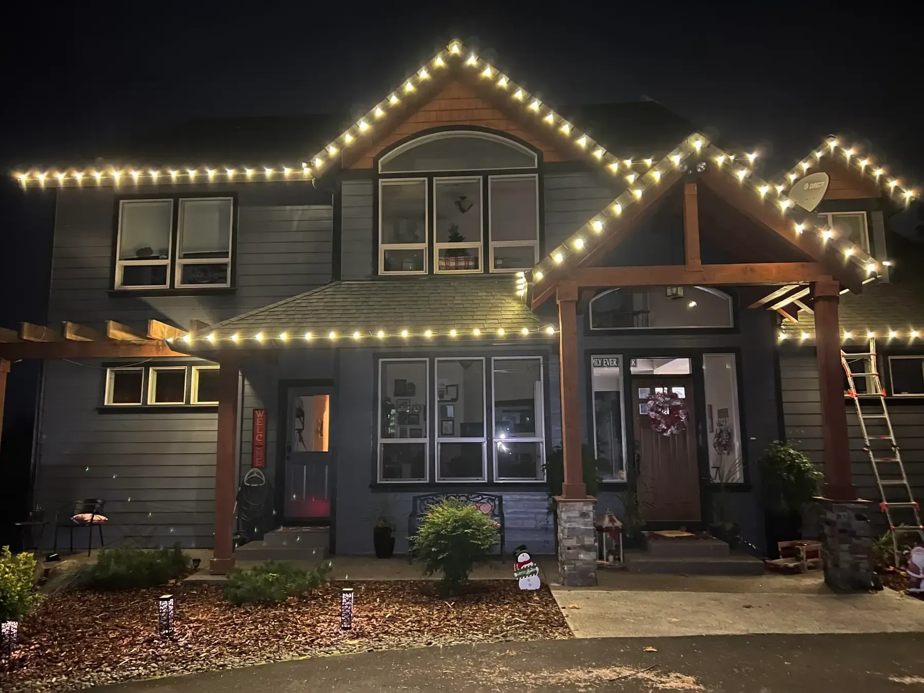 Two-story house at night outlined with warm white holiday lights and decorated front entry