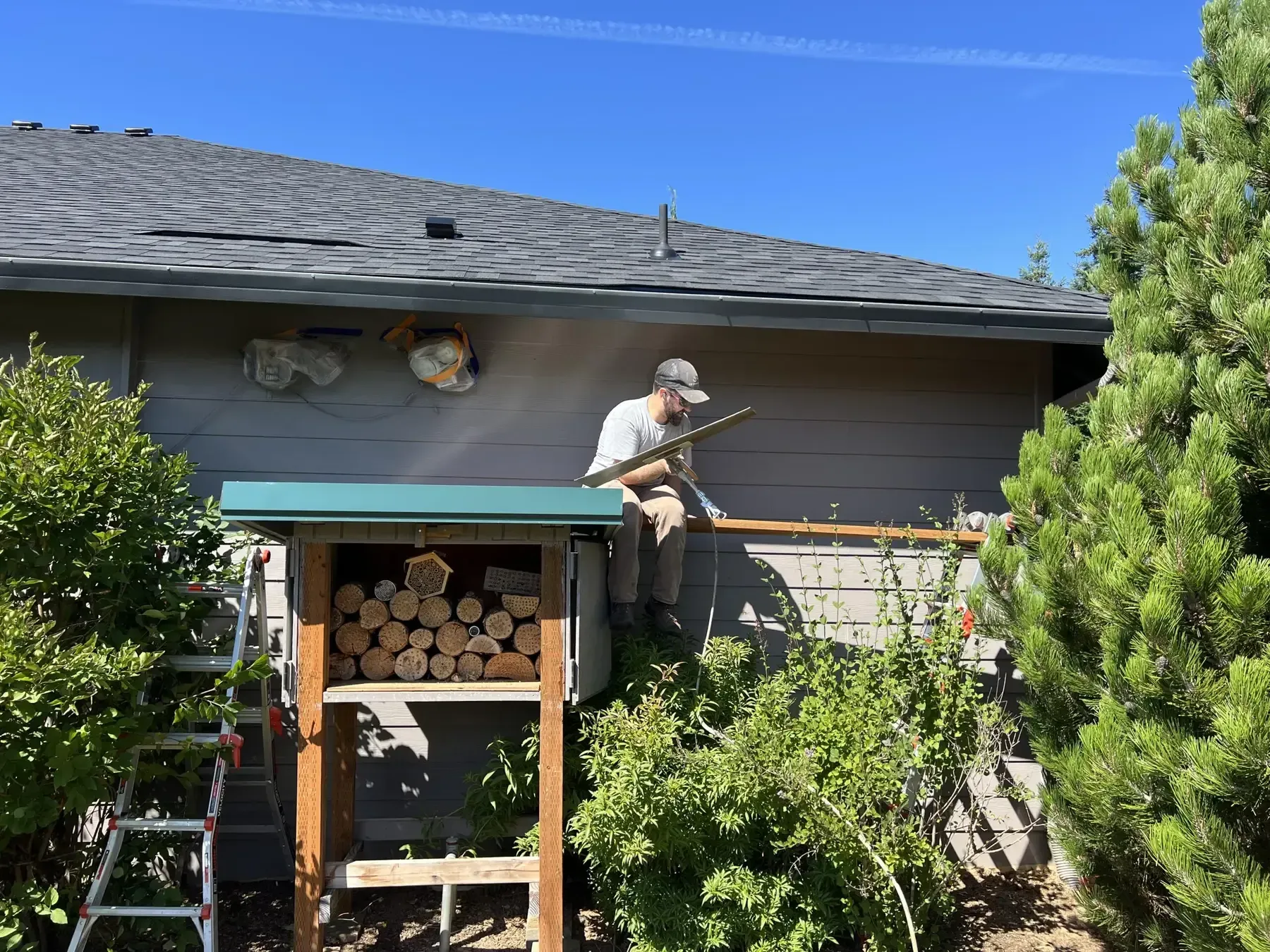 Person on a roof repairing shingles beside a woodpile under a blue sky