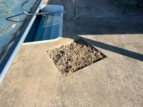 Pile of dirt on a concrete pool deck beside a blue swimming pool drain.