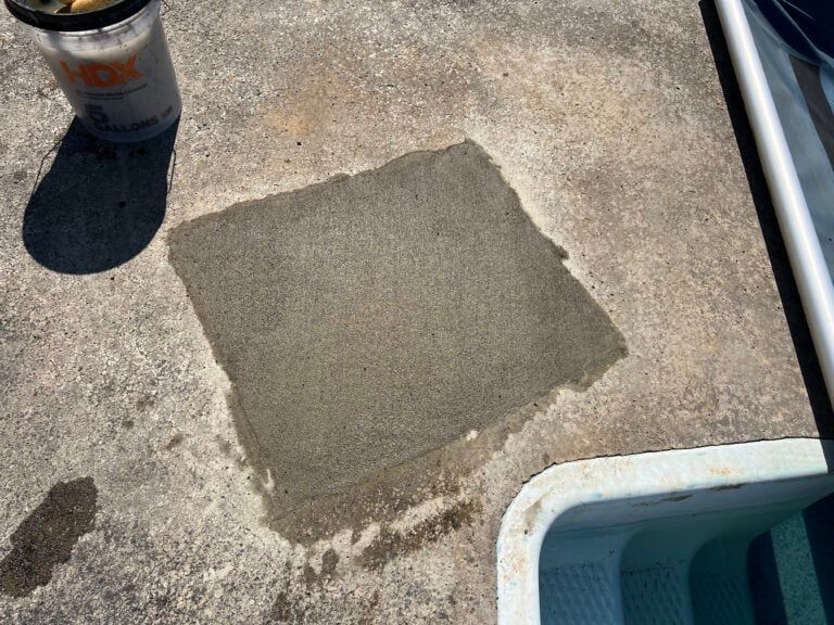 Square gray patch on a weathered concrete patio beside a blue cooler and a metal cup