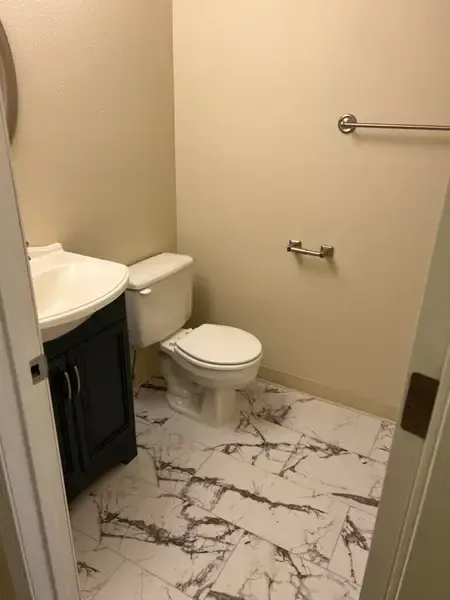 Small bathroom with toilet, sink vanity, towel bars, and marble-pattern tile floor.