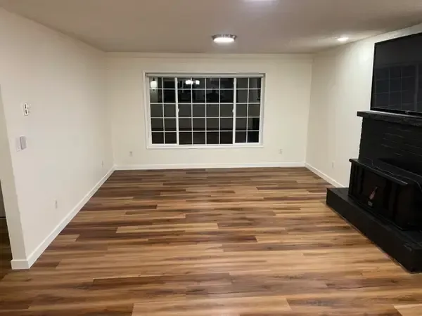 Empty living room with wood floors, white walls, a large window, and a black fireplace