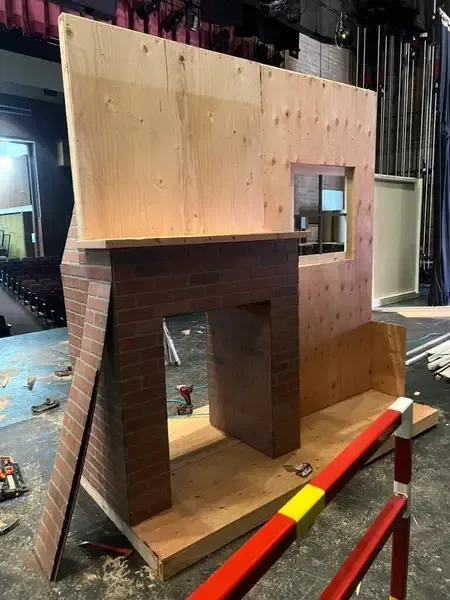 Partially built plywood kiosk with brick-textured front and a small window in a workshop