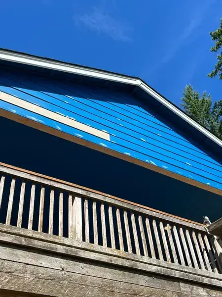 Blue house gable and weathered wooden balcony against a clear sky