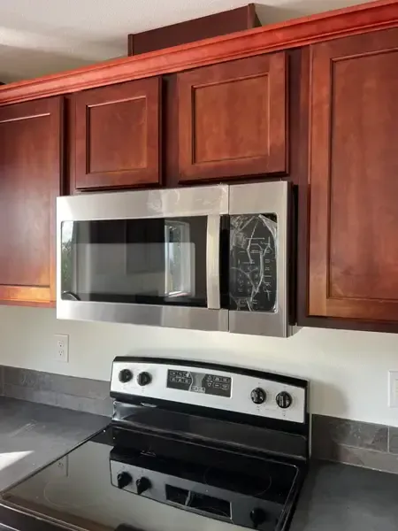 Kitchen with stainless steel microwave above a black electric range and dark wood cabinets