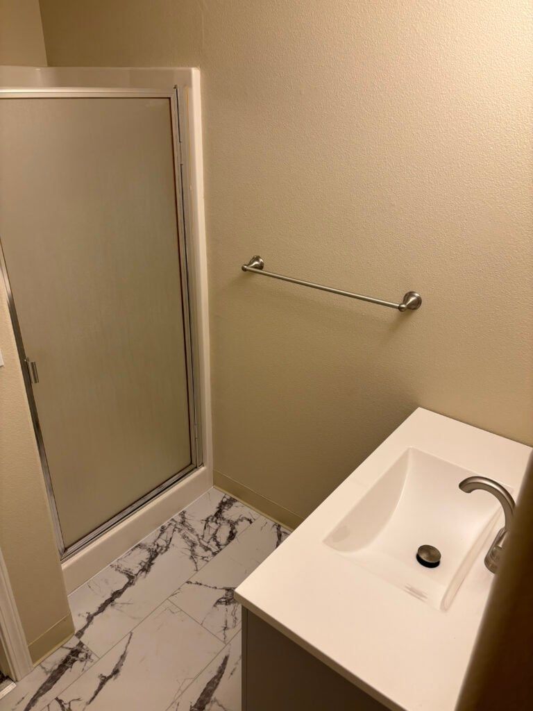 Small bathroom with shower, wall towel bar, and white sink with chrome faucet.