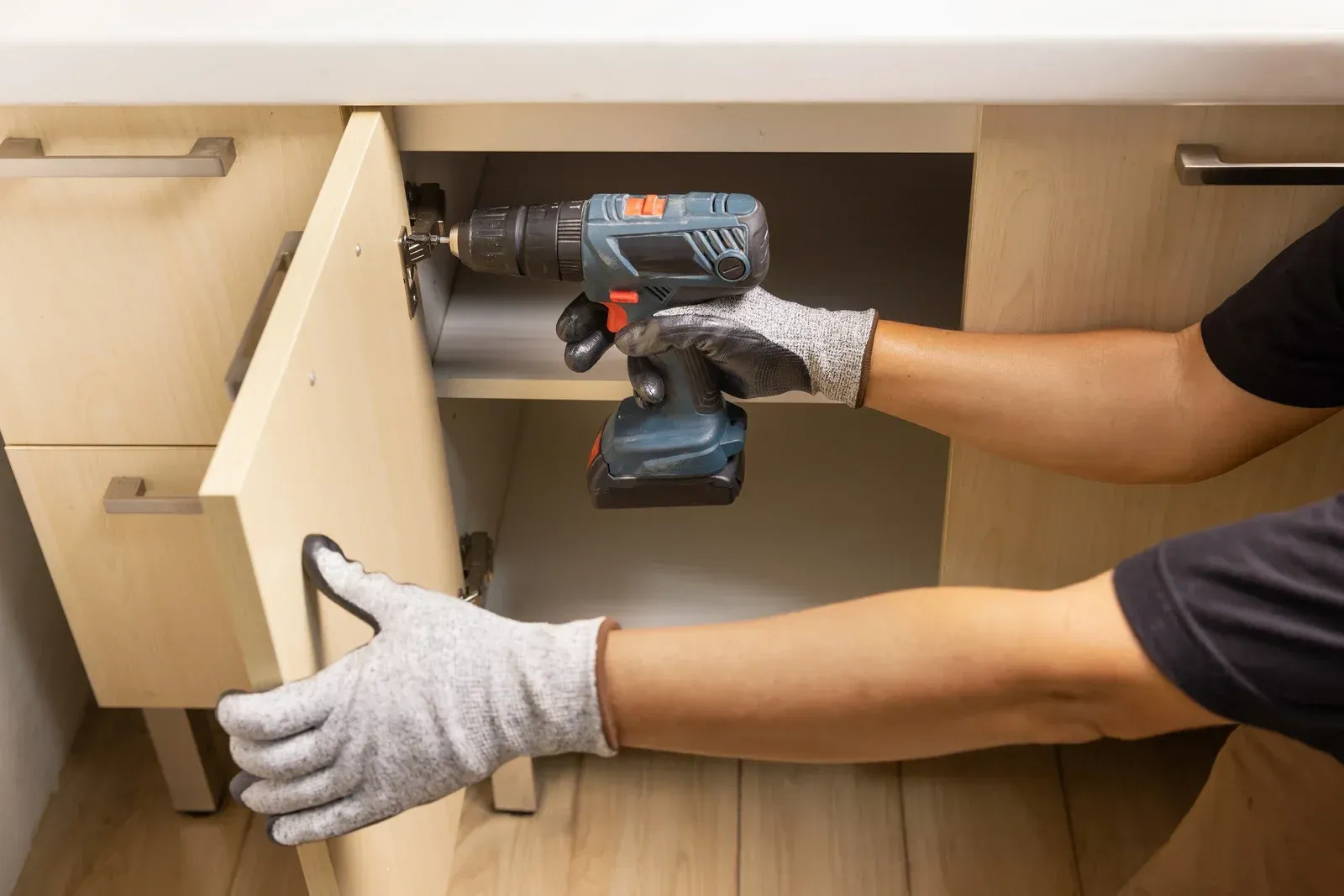 Person using a cordless drill to install a cabinet drawer in a kitchen.