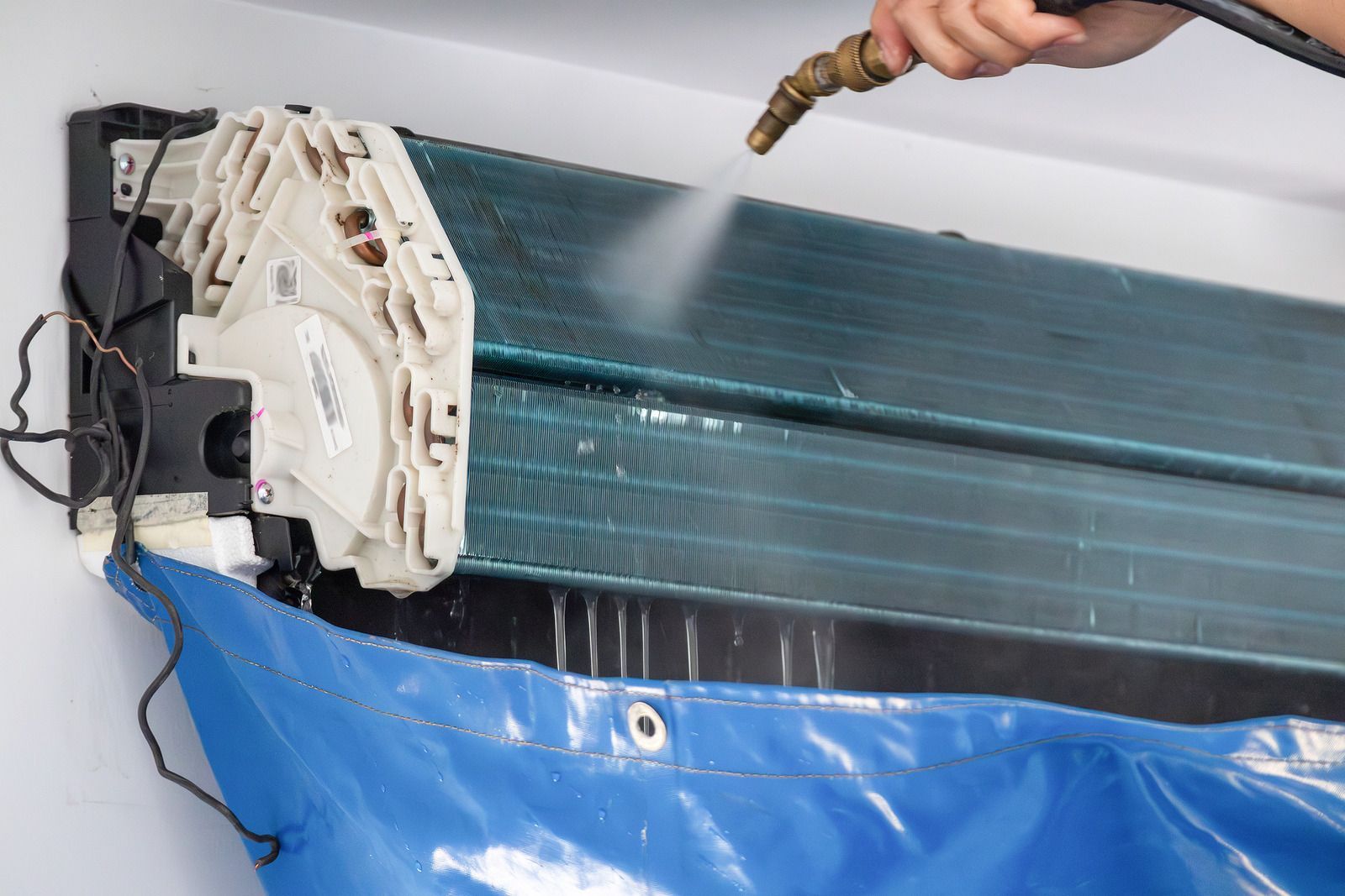 Cleaning an air conditioner unit with a hose, water spraying over the blue coil.