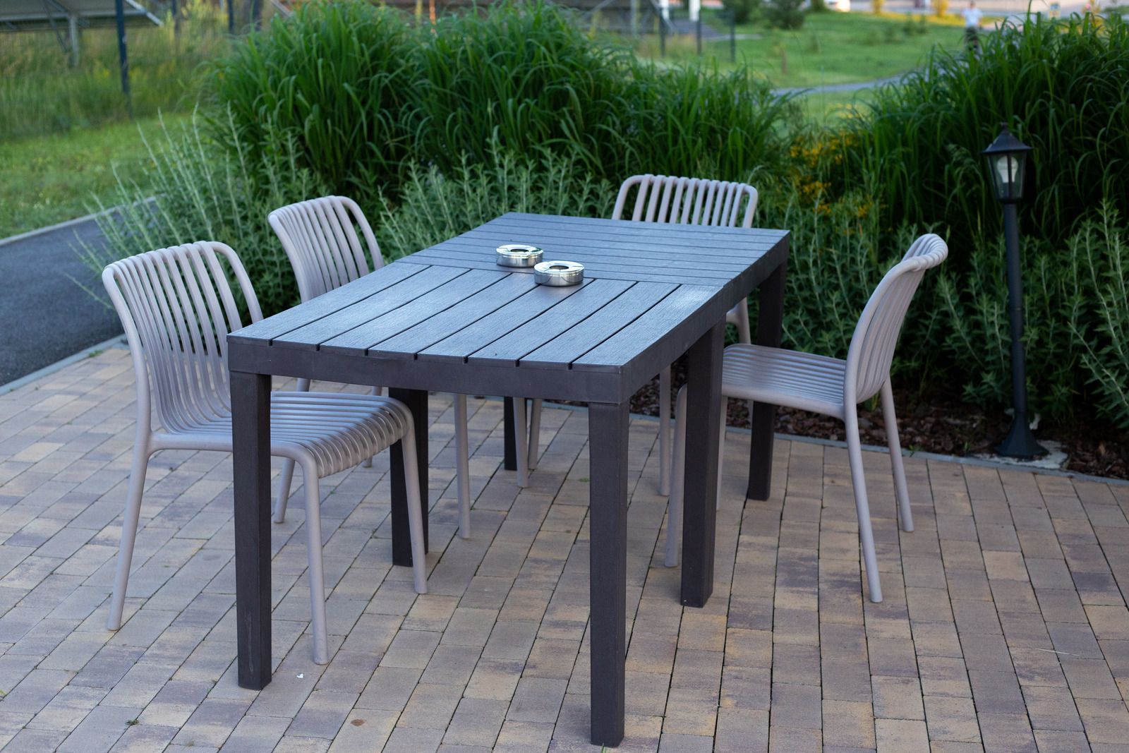 Outdoor patio dining table with four chairs and small bowls on top, beside a grassy garden path.