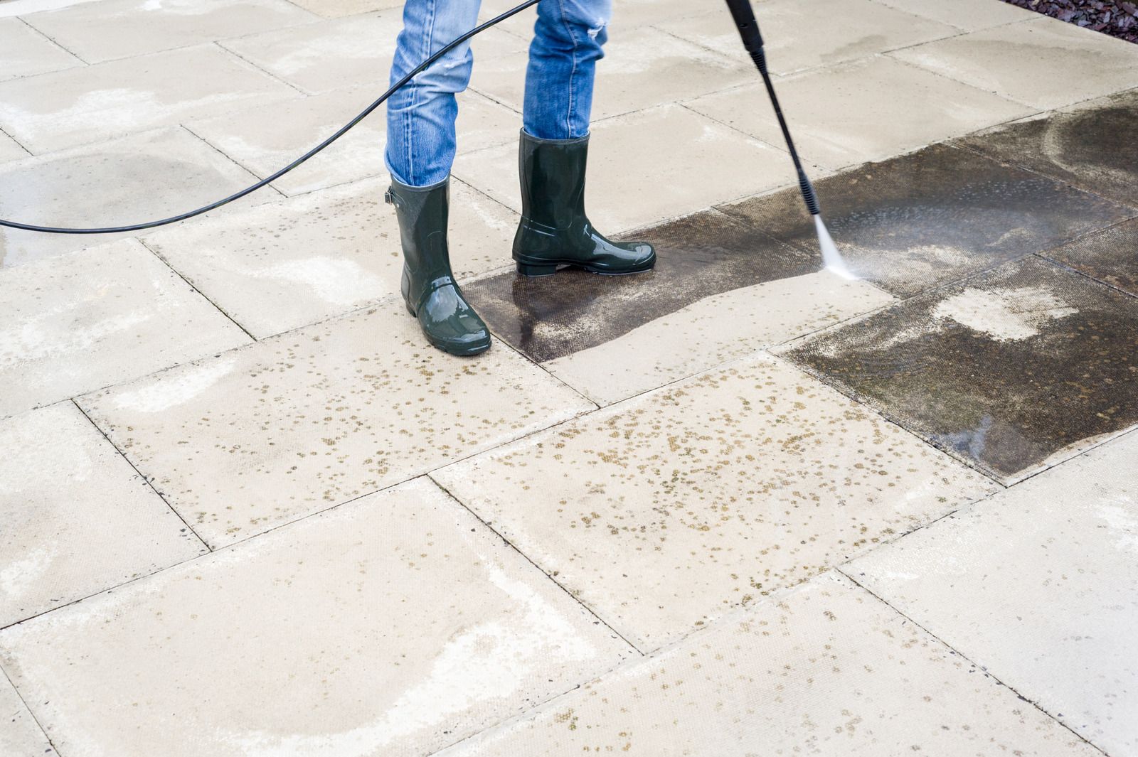 Person pressure washing a tiled pavement with a spray wand