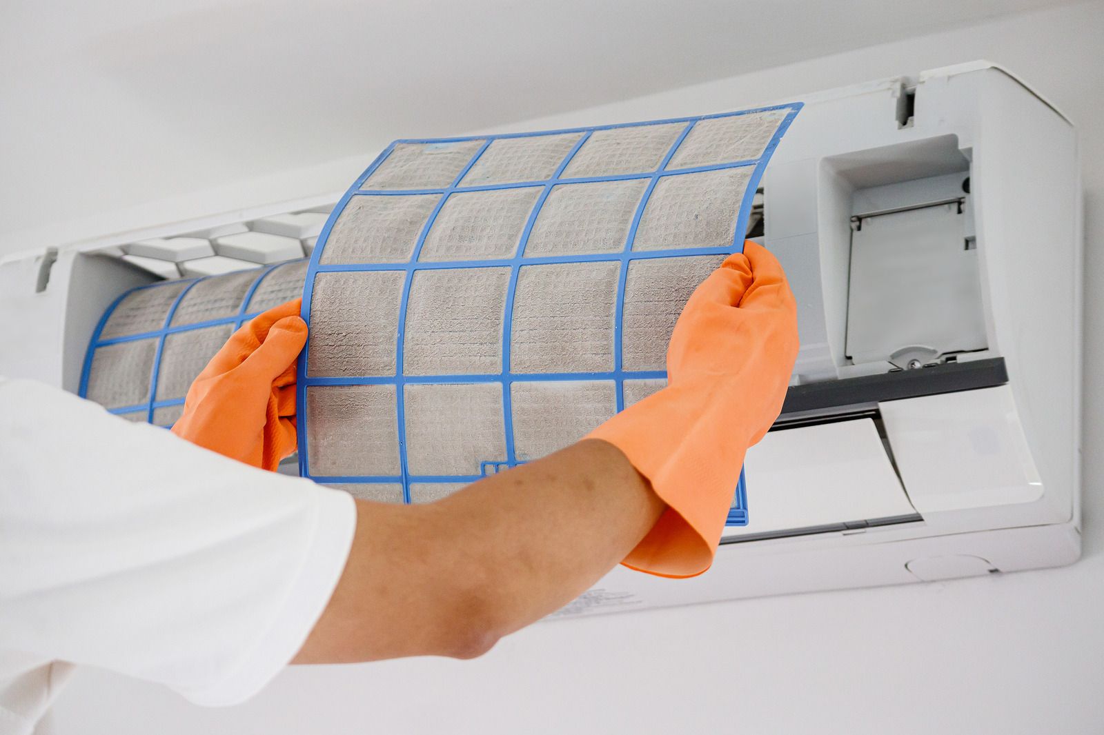 Technician replacing a blue air conditioner filter with orange gloves