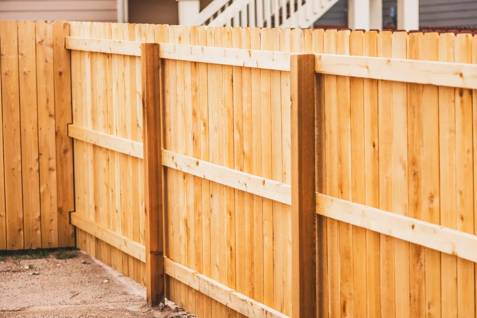 Wooden privacy fence with horizontal rails and a gate along a gravel path