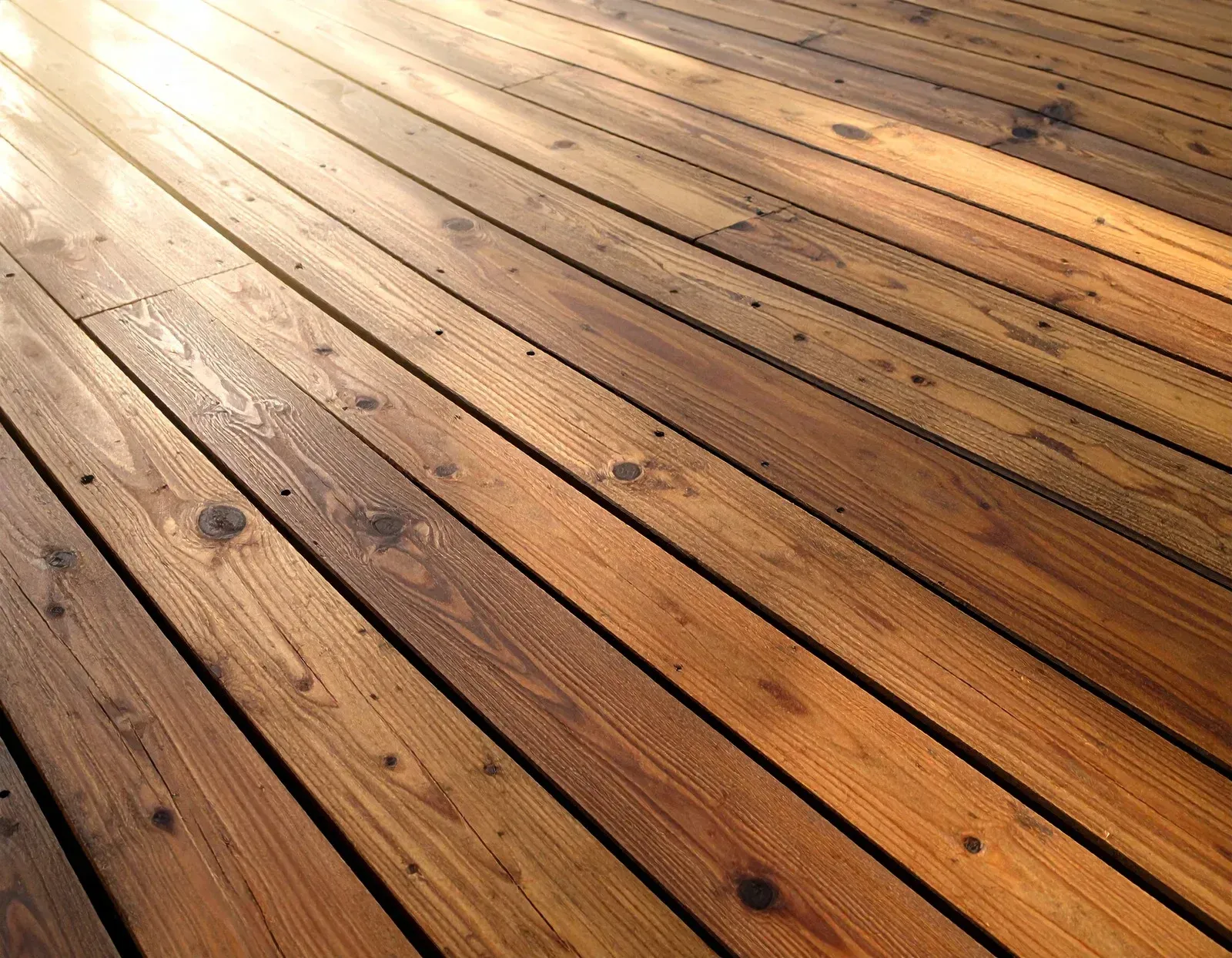 Sunlit wooden deck boards with a warm brown finish and visible knots