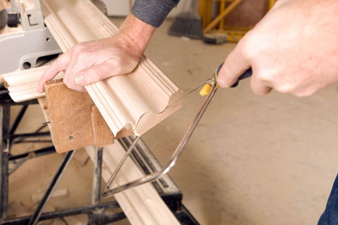 Hands cutting white trim with a saw in a workshop