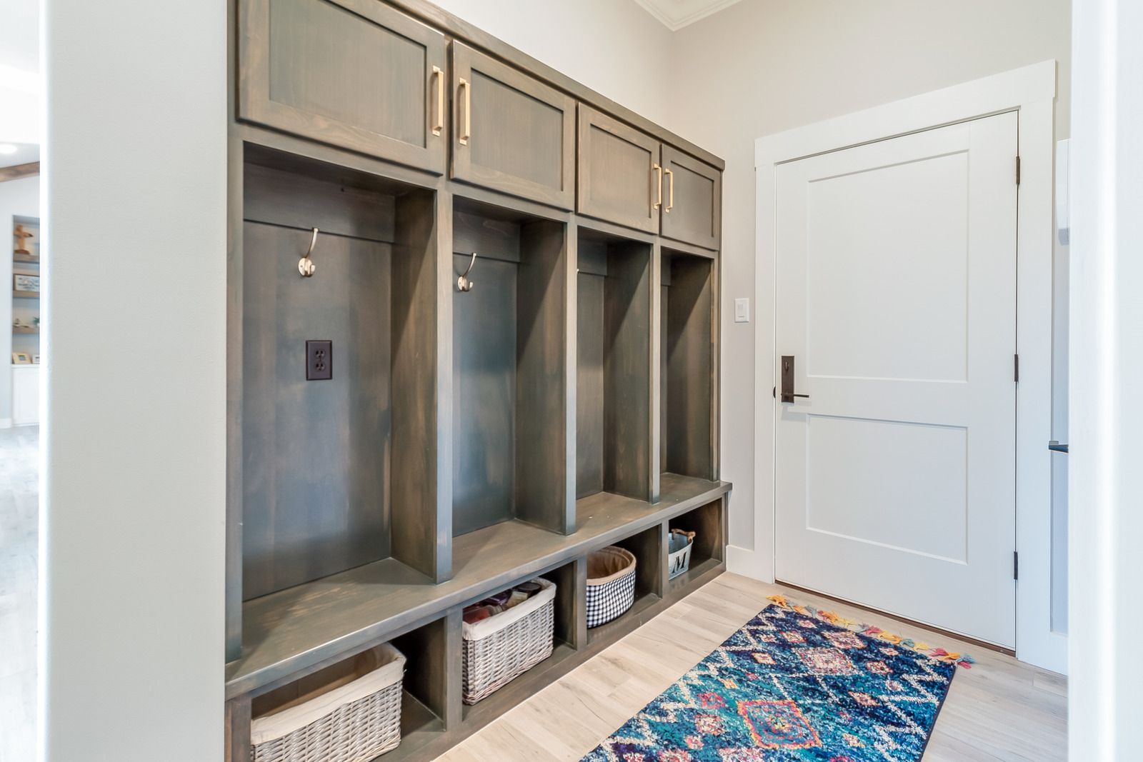 Built-in mudroom lockers with baskets and a colorful rug beside a white door