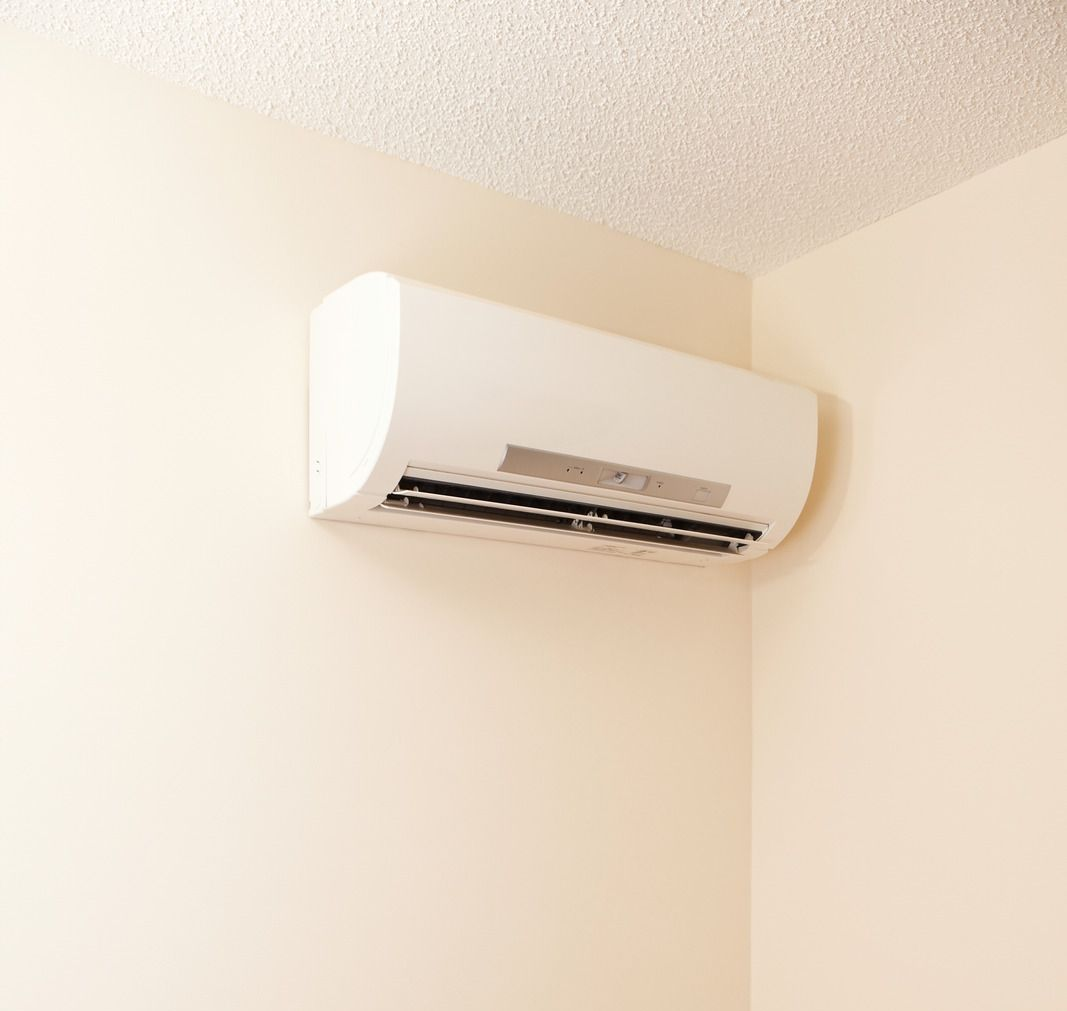 Wall-mounted white air conditioner in a beige corner room, near the ceiling