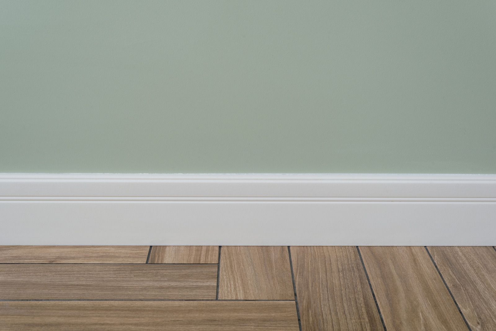 White baseboard against a pale green wall above wood flooring