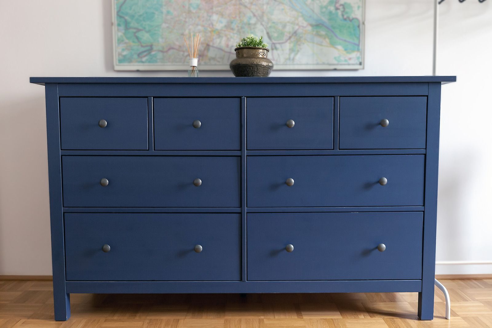 Blue dresser with eight drawers, a small plant on top, and a map hanging above it.
