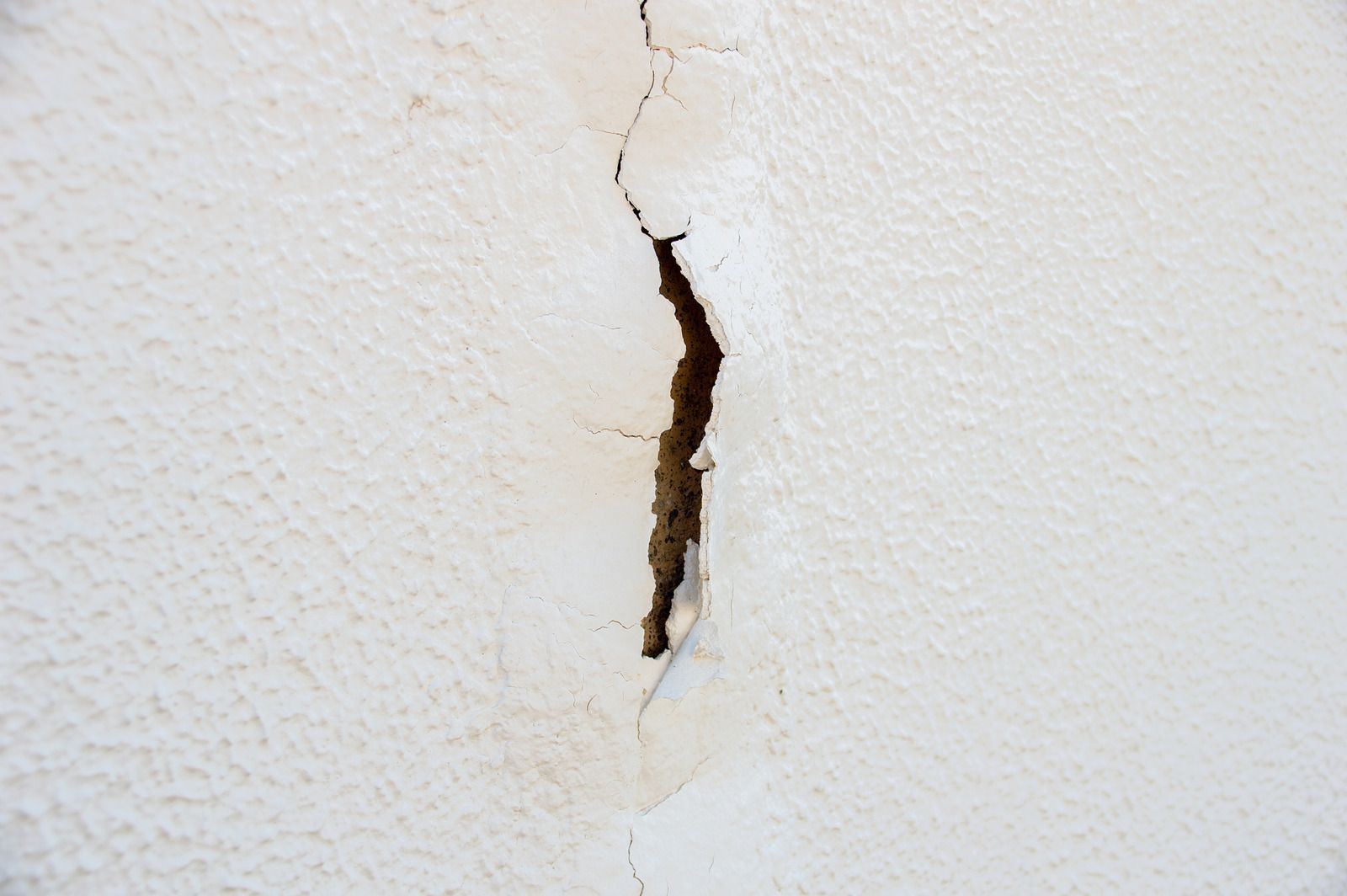 Cracked white wall with a narrow vertical split exposing dark damage