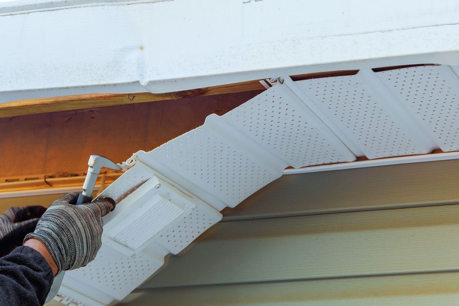 Gloved hand painting white soffit panels under a roof eave with a brush