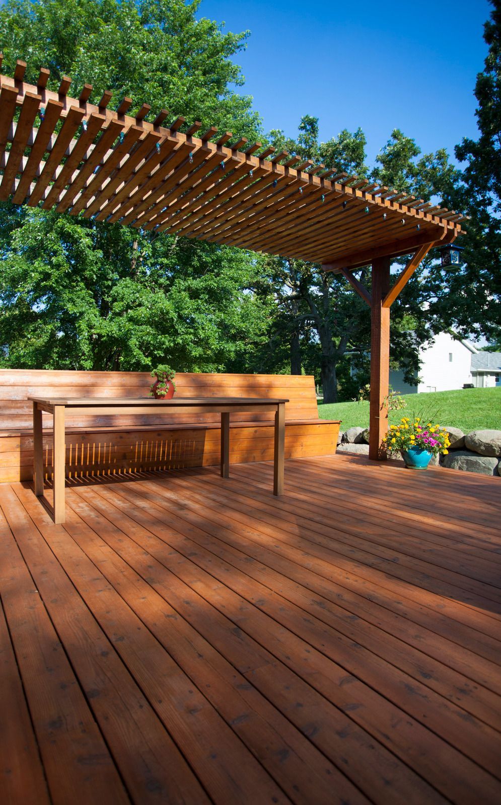 Wooden deck with pergola, built-in bench, and a small table under a sunny blue sky.