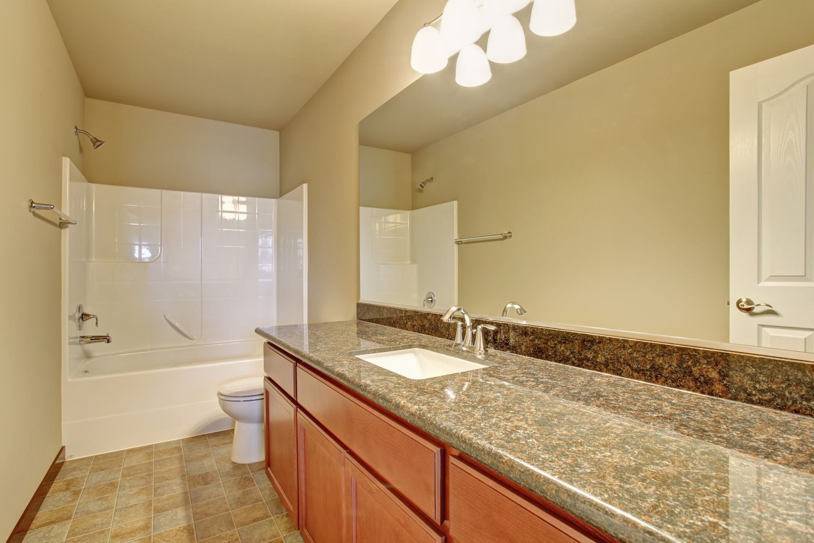 Modern bathroom with granite vanity, large mirror, and white tub-shower combo