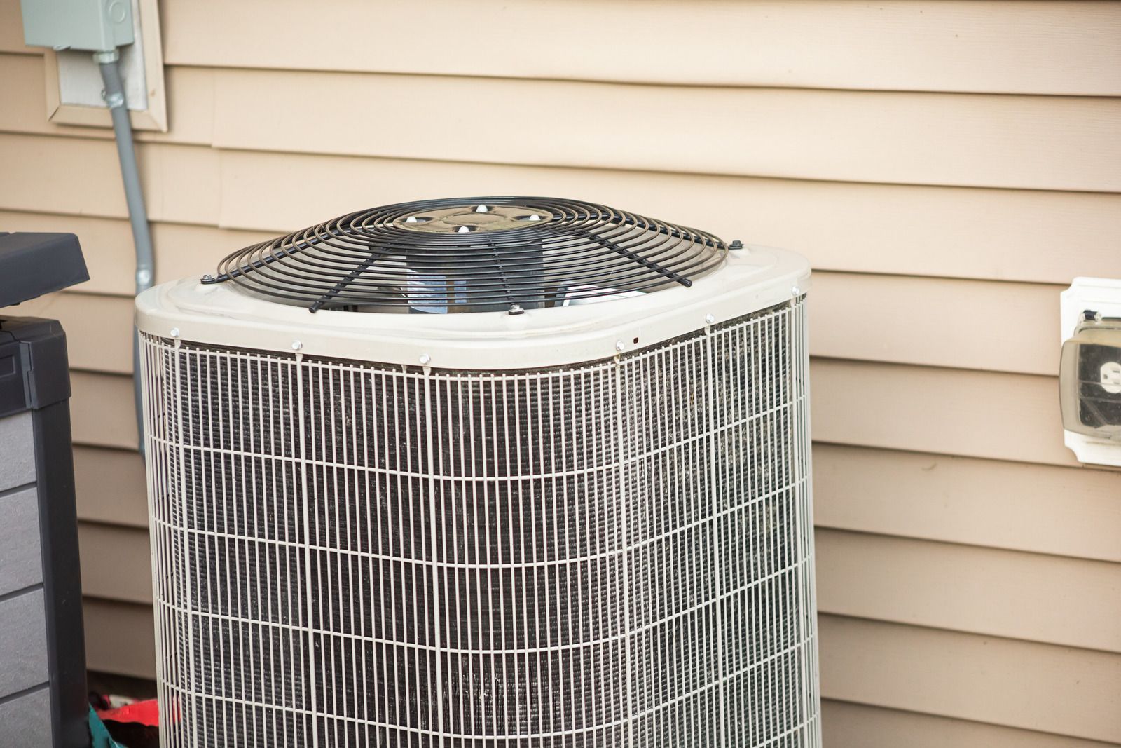 Outdoor air conditioner unit beside tan house siding