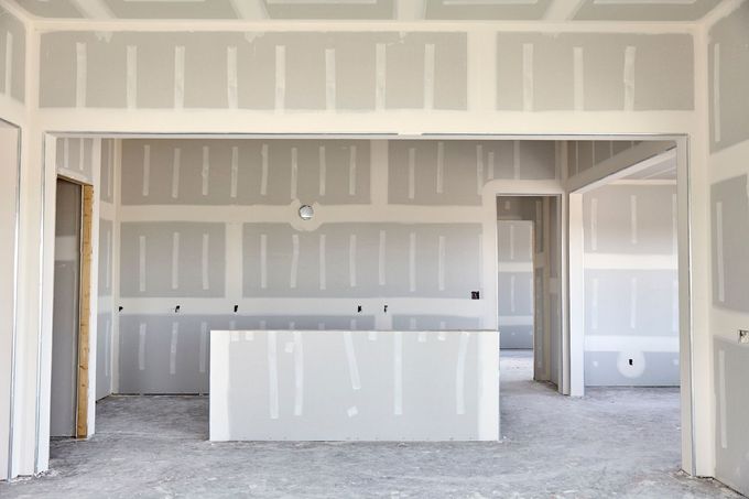 Unfinished kitchen interior with drywall, white island, and exposed openings to adjacent rooms.