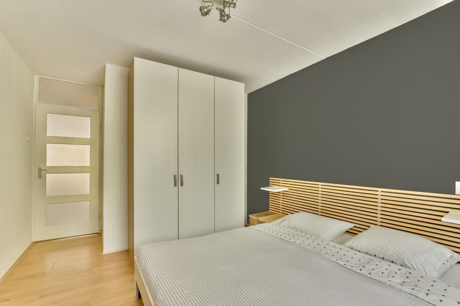Modern bedroom with gray accent wall, white wardrobe, and bed with woven headboard