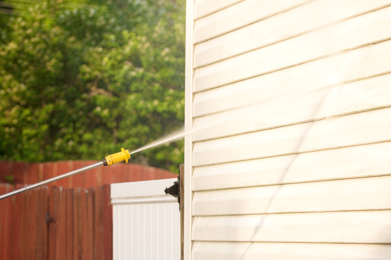 Yellow cable stretched to a white house wall beside a fence and trees