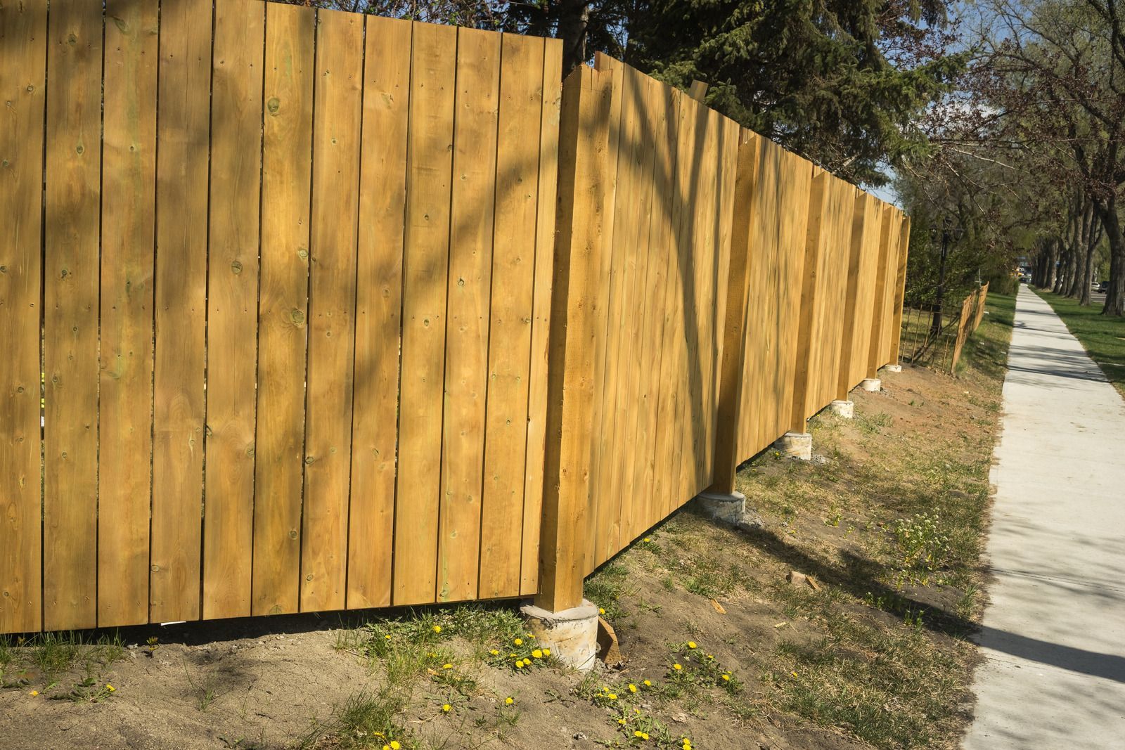 Wooden fence along a sidewalk beside a grassy roadside area