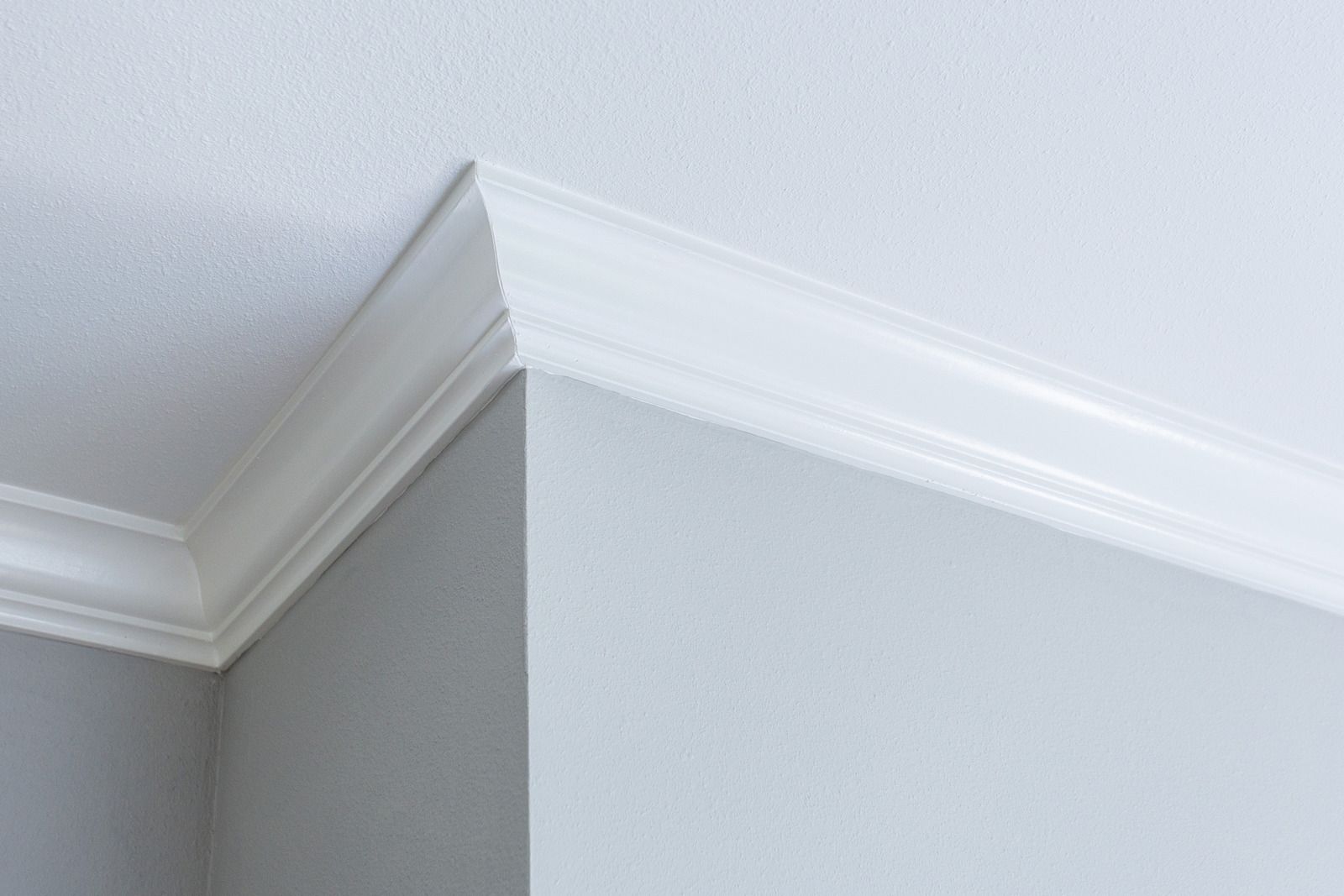 Corner of a room with white crown molding and a gray wall near a white ceiling