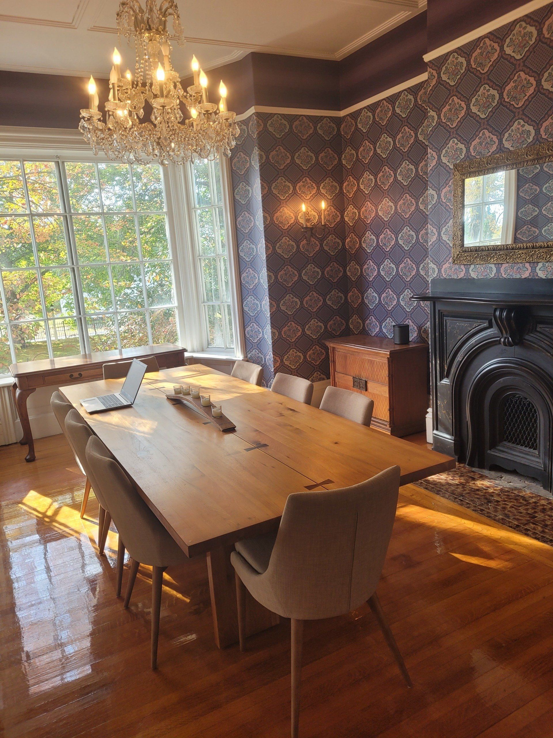 A dining room with a long wooden table and chairs and a fireplace.