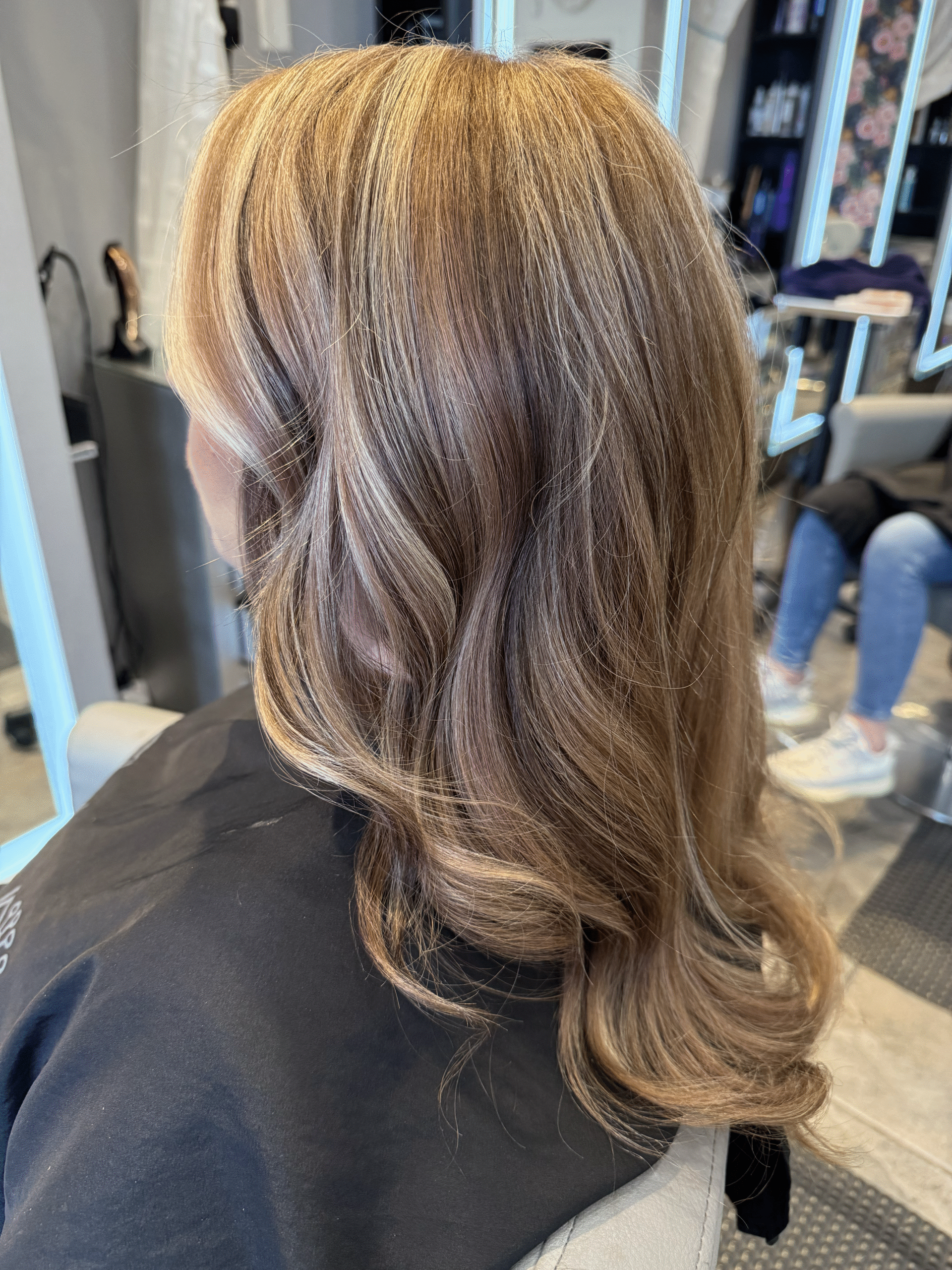 Brown wavy shoulder-length hair with subtle highlights, viewed from behind in a salon chair