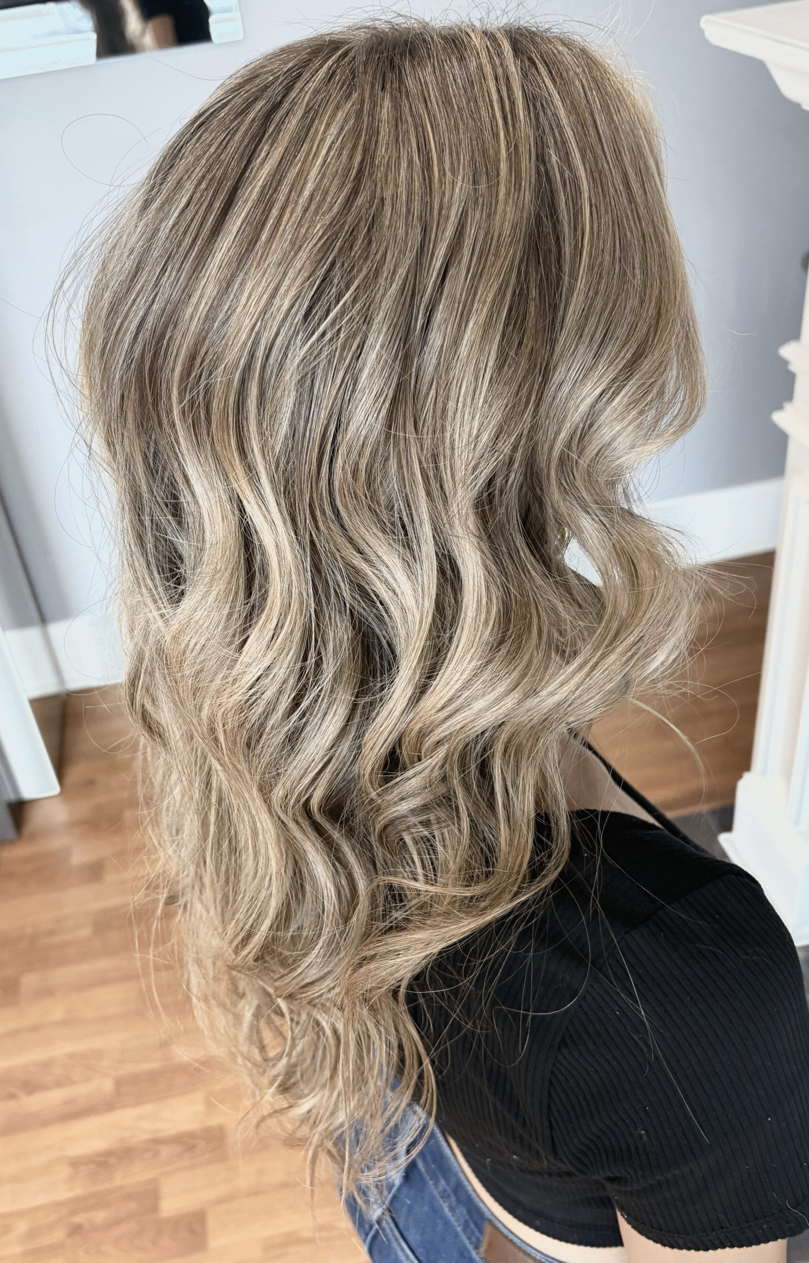 Wavy blonde highlights on shoulder-length layered hair, viewed from the back in a salon setting