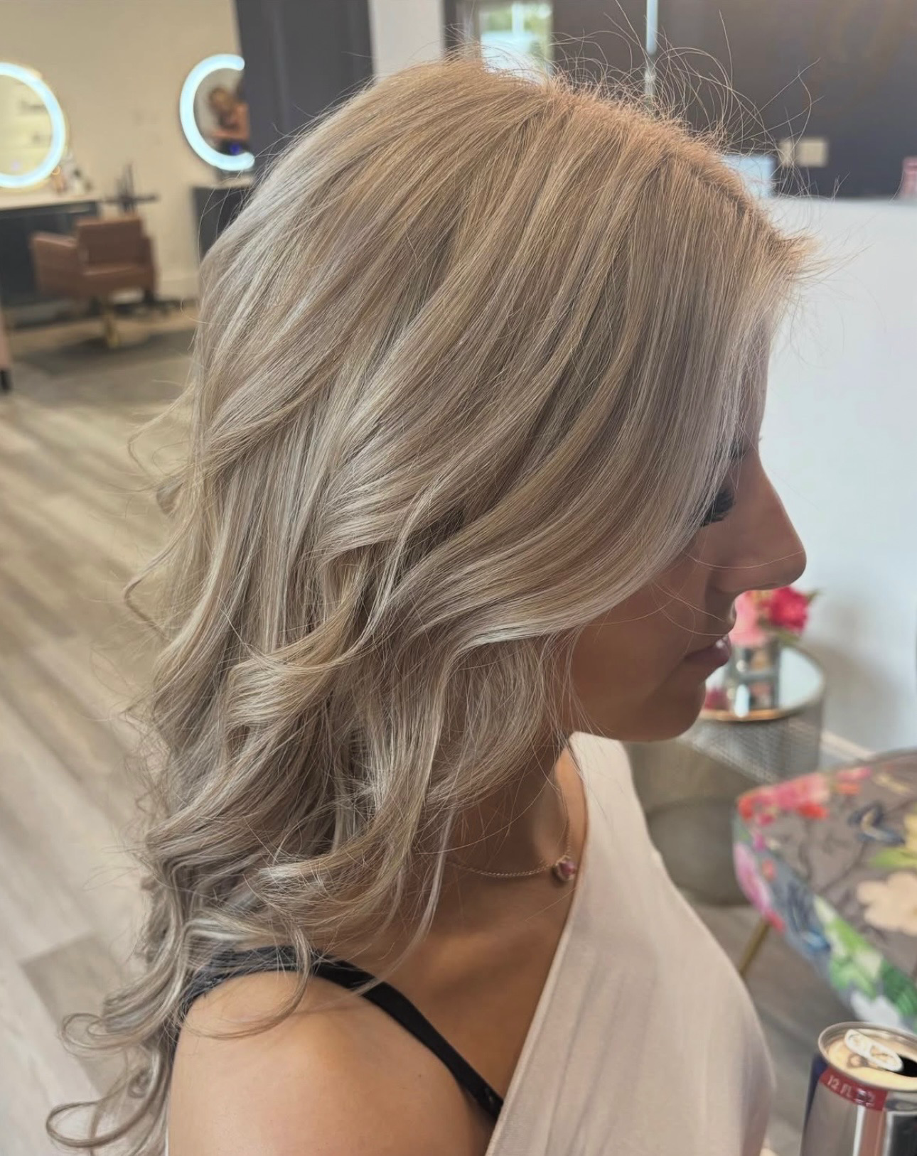 Side view of a woman with wavy blonde hair in a salon, wearing a white top