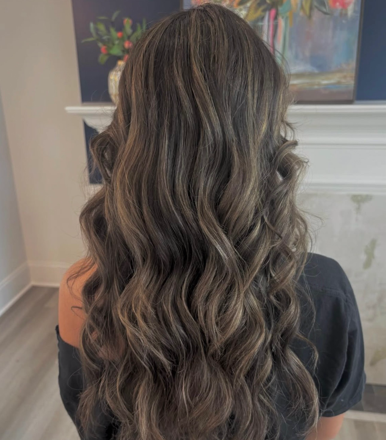 Long wavy brunette hair with caramel highlights, shown from behind in a salon setting