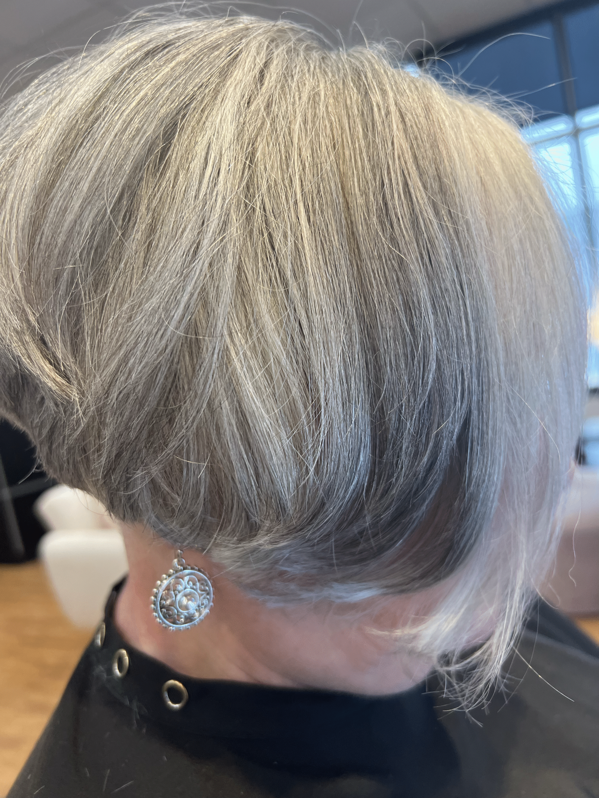 Short silver-blonde haircut with dark underlayers and a dangling earring in a café setting