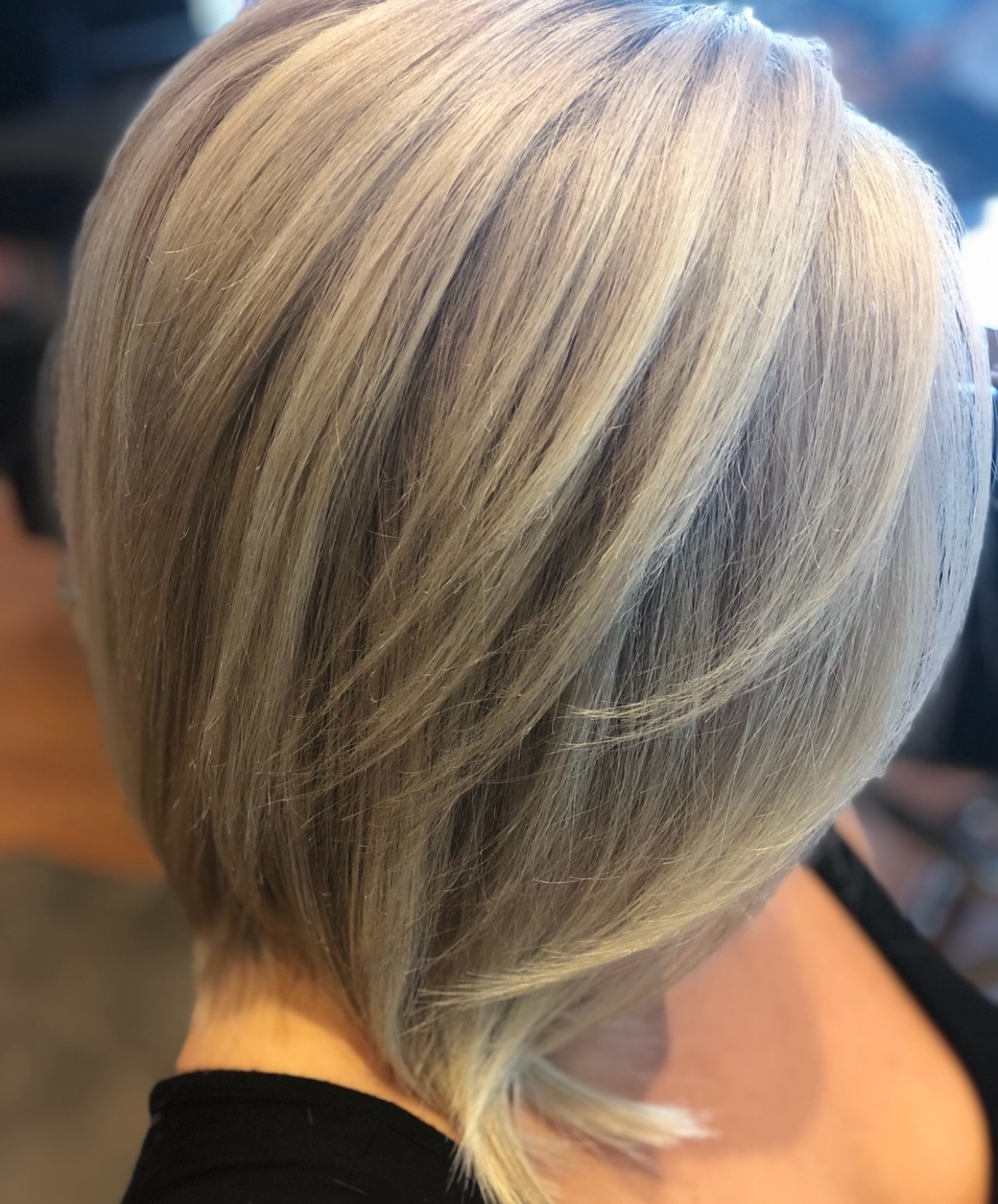 Short layered silver-blonde haircut with darker roots, viewed from the back in a salon setting