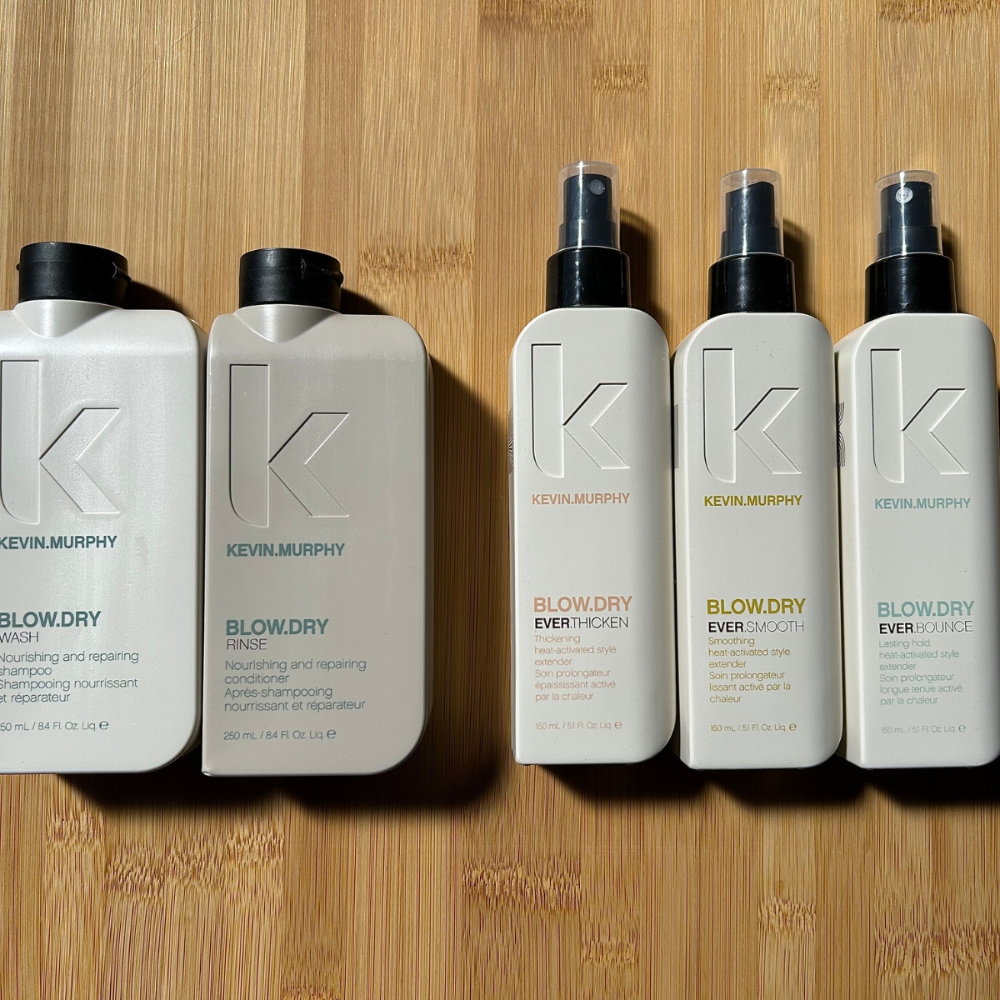 Three cosmetic tubes and bottles on a gray surface, in beige, white, and tan packaging.