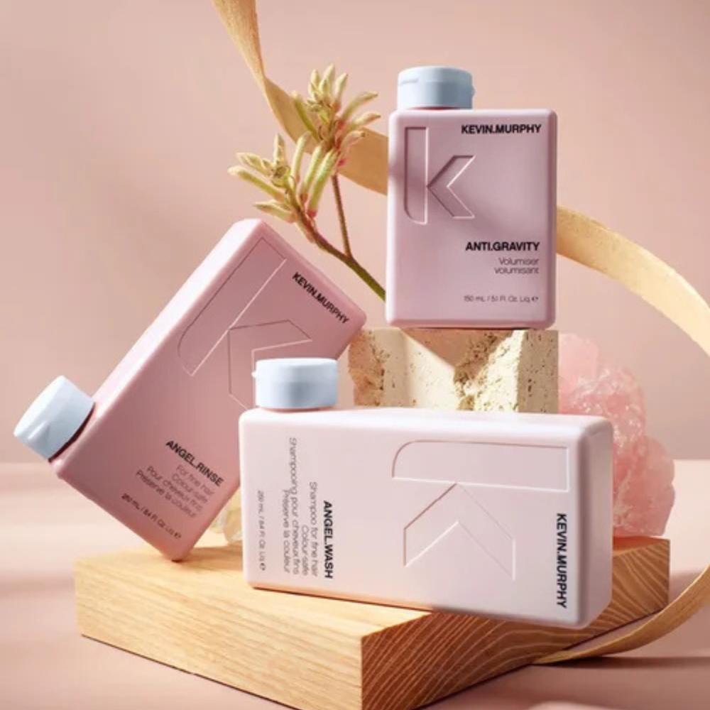 Four KÉUNE hair care product bottles in white and amber on a light beige background