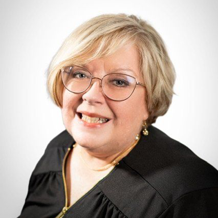 Portrait of a smiling person with short blond hair and glasses, wearing a black top on a white background