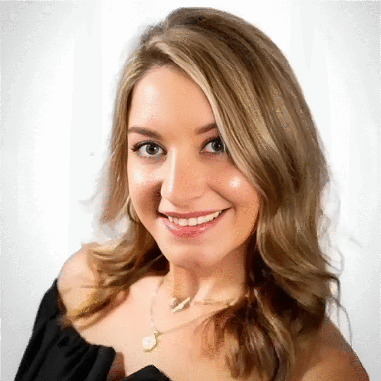 Smiling woman with wavy blonde hair wearing a black top and gold necklace on a white background