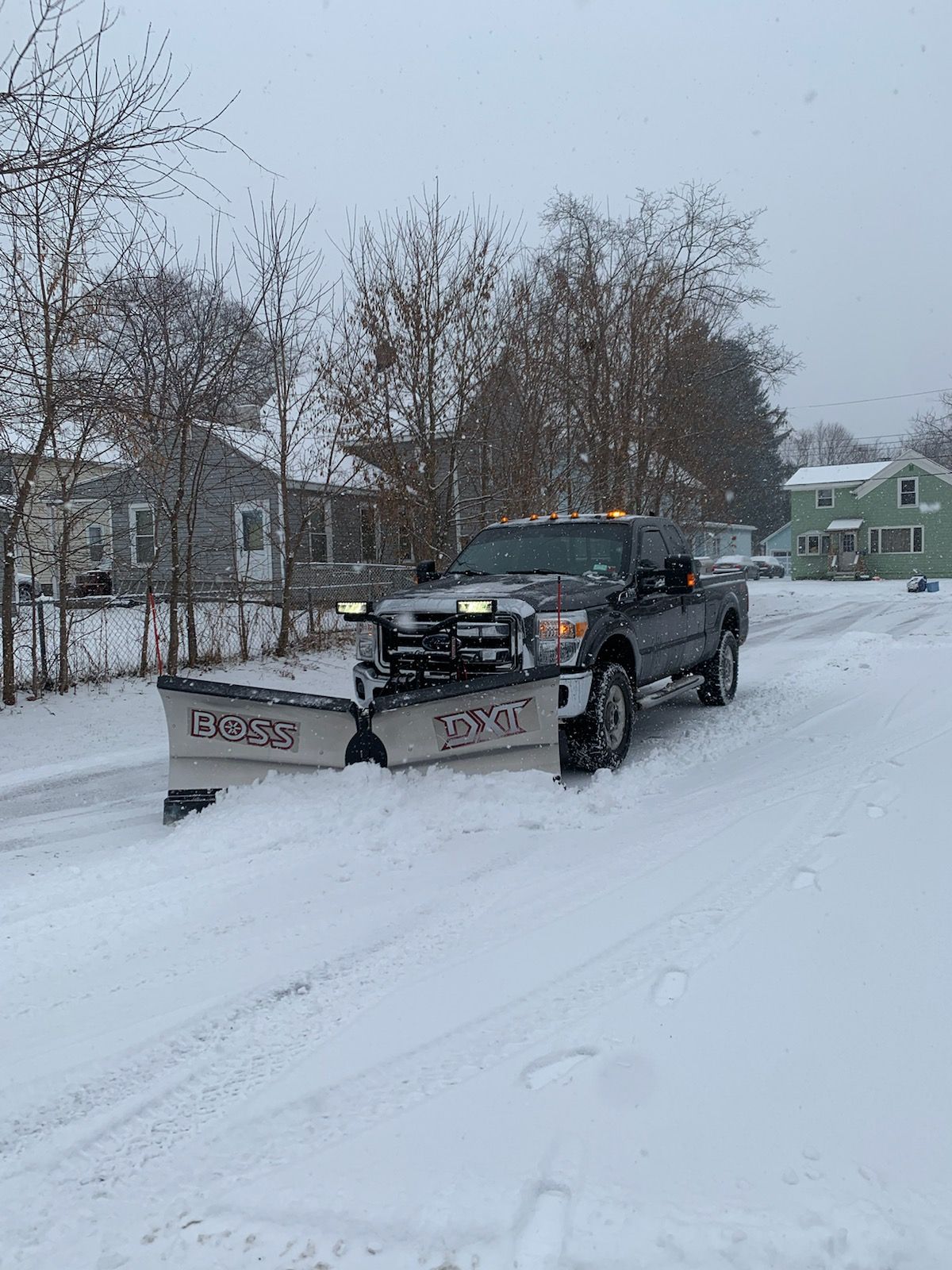 A truck with a snow plow attached to it is driving down a snowy street.