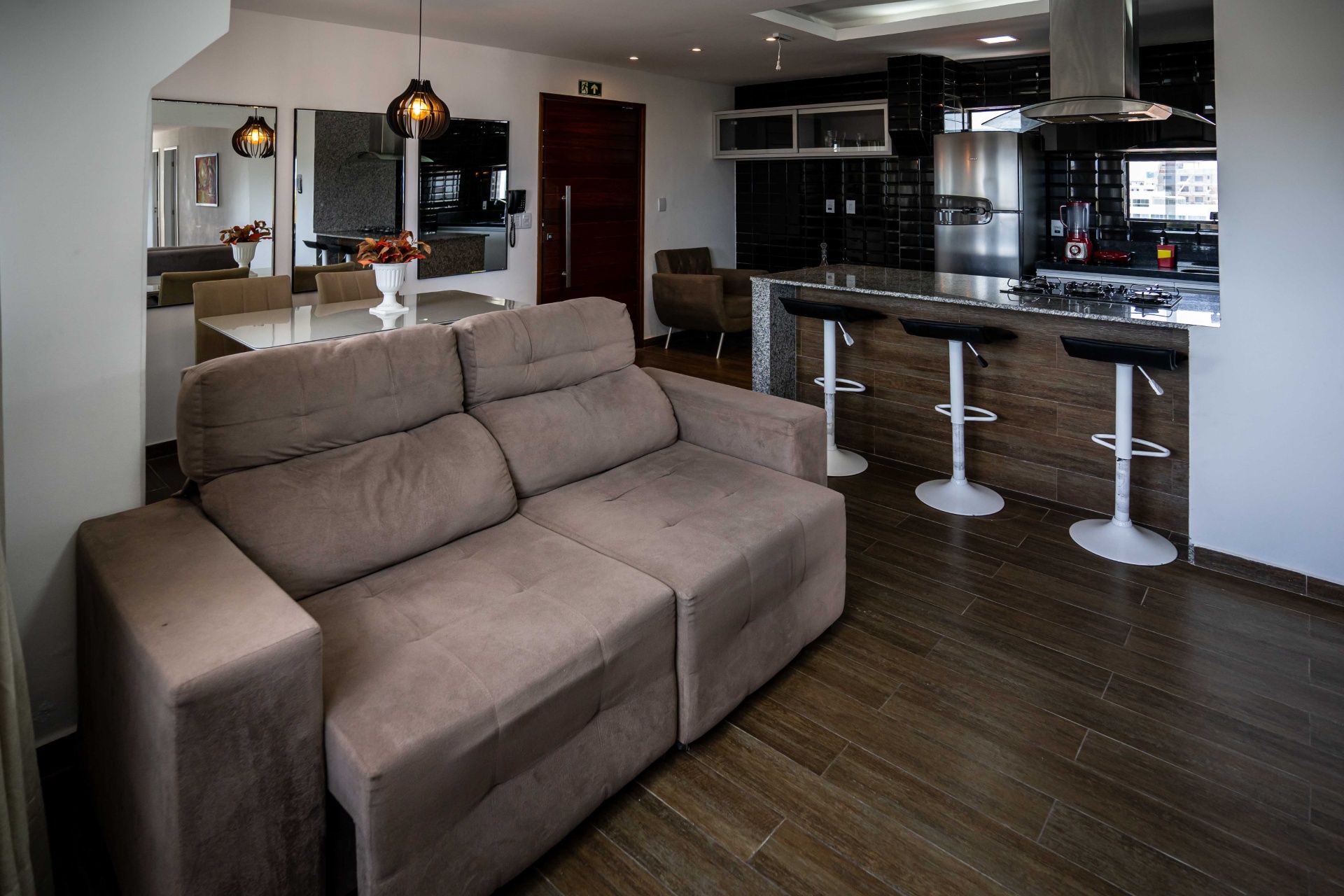Sala de estar moderna em conceito aberto com sofá cinza, piso de madeira escura e ilha de cozinha com banquetas.