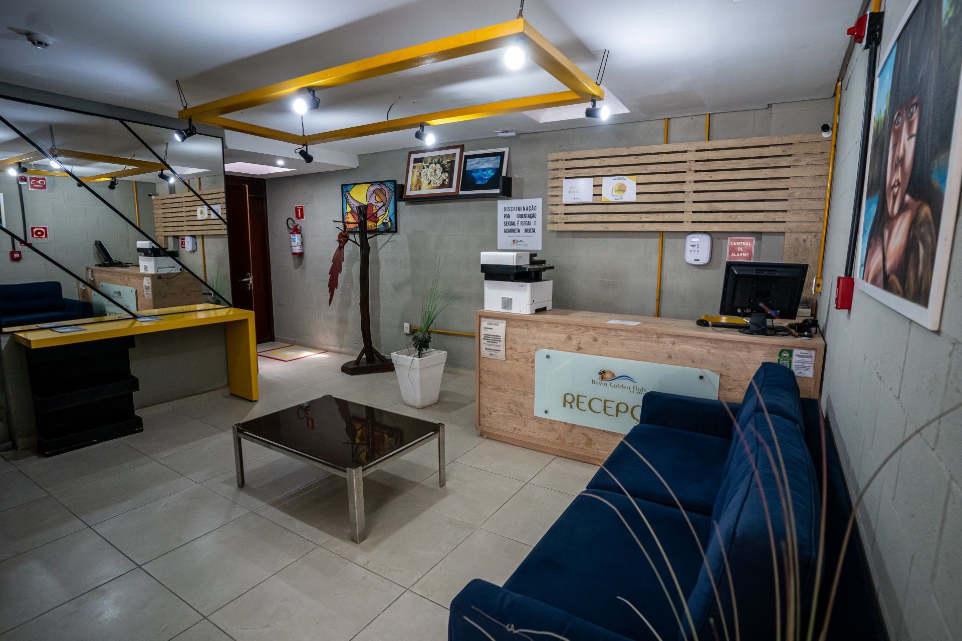 Hall de entrada de escritório moderno com sofá azul, balcão de recepção, mesa de centro e obras de arte na parede.