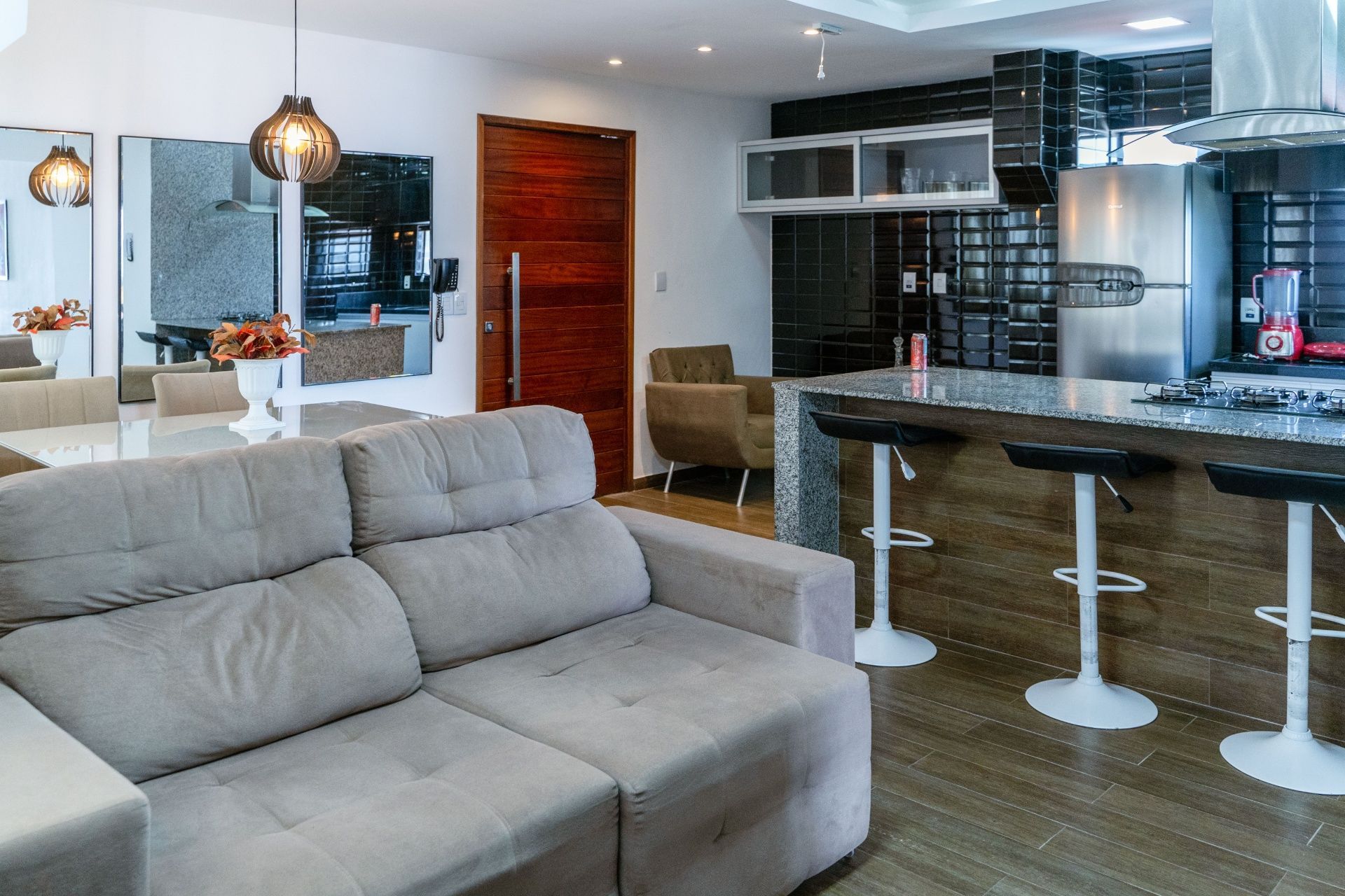 Sala de estar moderna de conceito aberto com sofá modular cinza, ilha de cozinha e banquetas de bar.